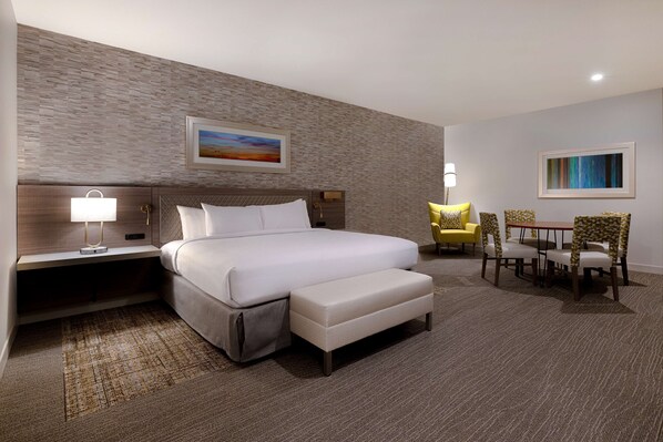 A hotel room with a large bed, a bedside table with a lamp, a small table with chairs, and a painting on the wall.