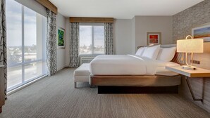 A modern hotel room with a large bed, a bedside table with a lamp, a window with curtains, and artwork on the walls. - Hilton Garden Inn Temecula, CA (Temecula)