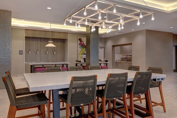 A modern dining area with a large rectangular table, six wicker chairs, and a unique ceiling light fixture.