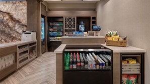 A modern hotel lobby with a marble wall, wooden flooring, and a refrigerated display case with beverages. - Hilton Garden Inn Temecula, CA (Temecula)