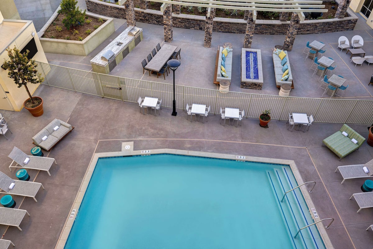 A rooftop pool area with lounge chairs, a pool, and a seating area with tables and chairs.
