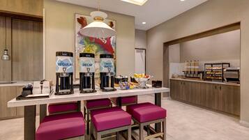 A modern kitchen area with a long counter, multiple coffee machines, and a fruit bowl.