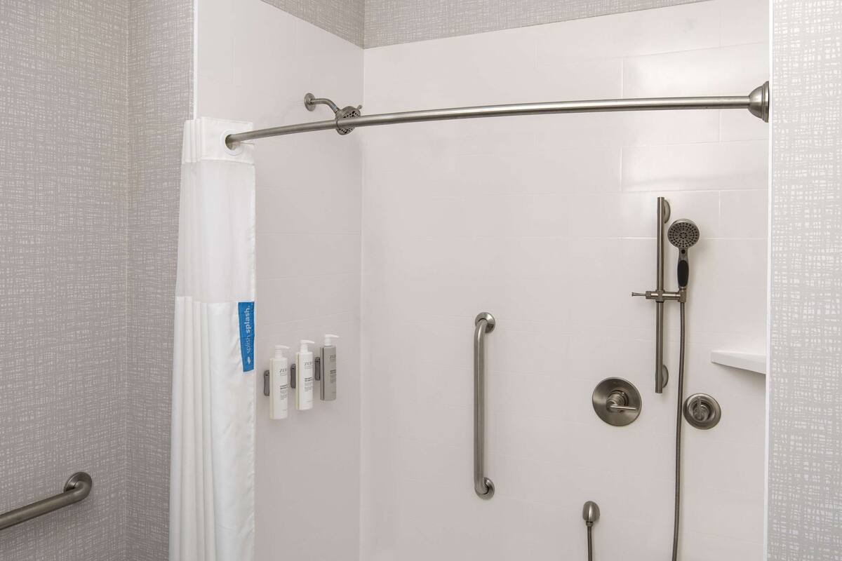 A modern shower area with a glass door, a handheld showerhead, a handheld shower nozzle, and a small shelf with toiletries.
