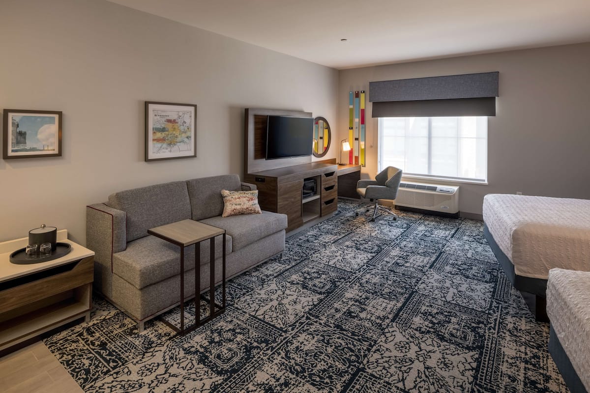 A modern hotel room with a sofa, a TV, a desk, and a bed.