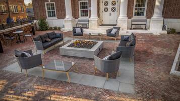 An outdoor patio with wicker furniture, a fire pit, and a brick building with columns.