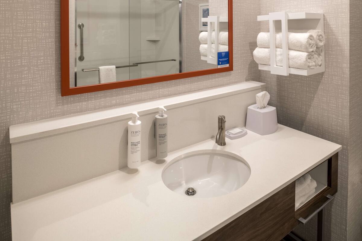A modern bathroom with a white sink, a mirror with a wooden frame, and a towel rack with neatly folded towels.