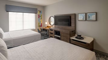 Habitación de hotel con dos camas, un escritorio con televisor de pantalla plana, un espejo redondo pequeño y una mesita de noche con lámpara.