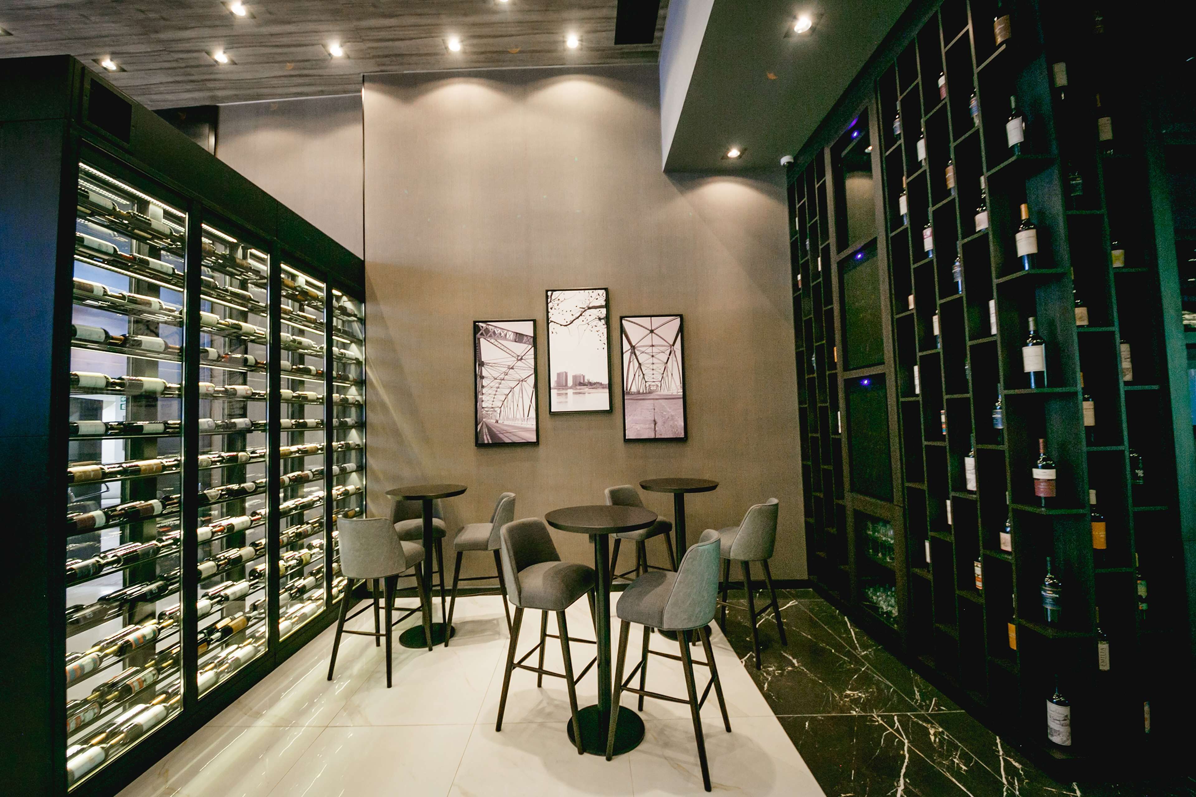 A wine cellar with shelves of bottles, a few tables with chairs, and framed pictures on the wall.