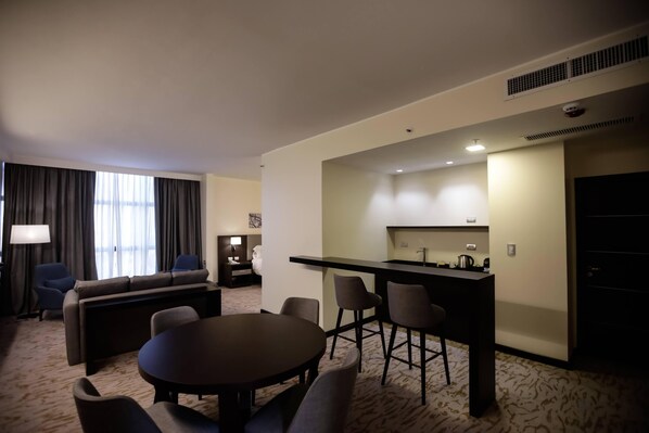 Habitación de hotel con sala de estar, mesa de comedor, cocina y sofá.