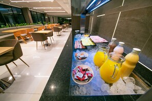 A breakfast bar with various food items and beverages, surrounded by seating and a modern interior. - Hilton Garden Inn Santiago del Estero (Santiago del Estero)