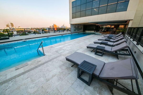 Un área de piscina en la azotea con sillones y vistas del horizonte de la ciudad.