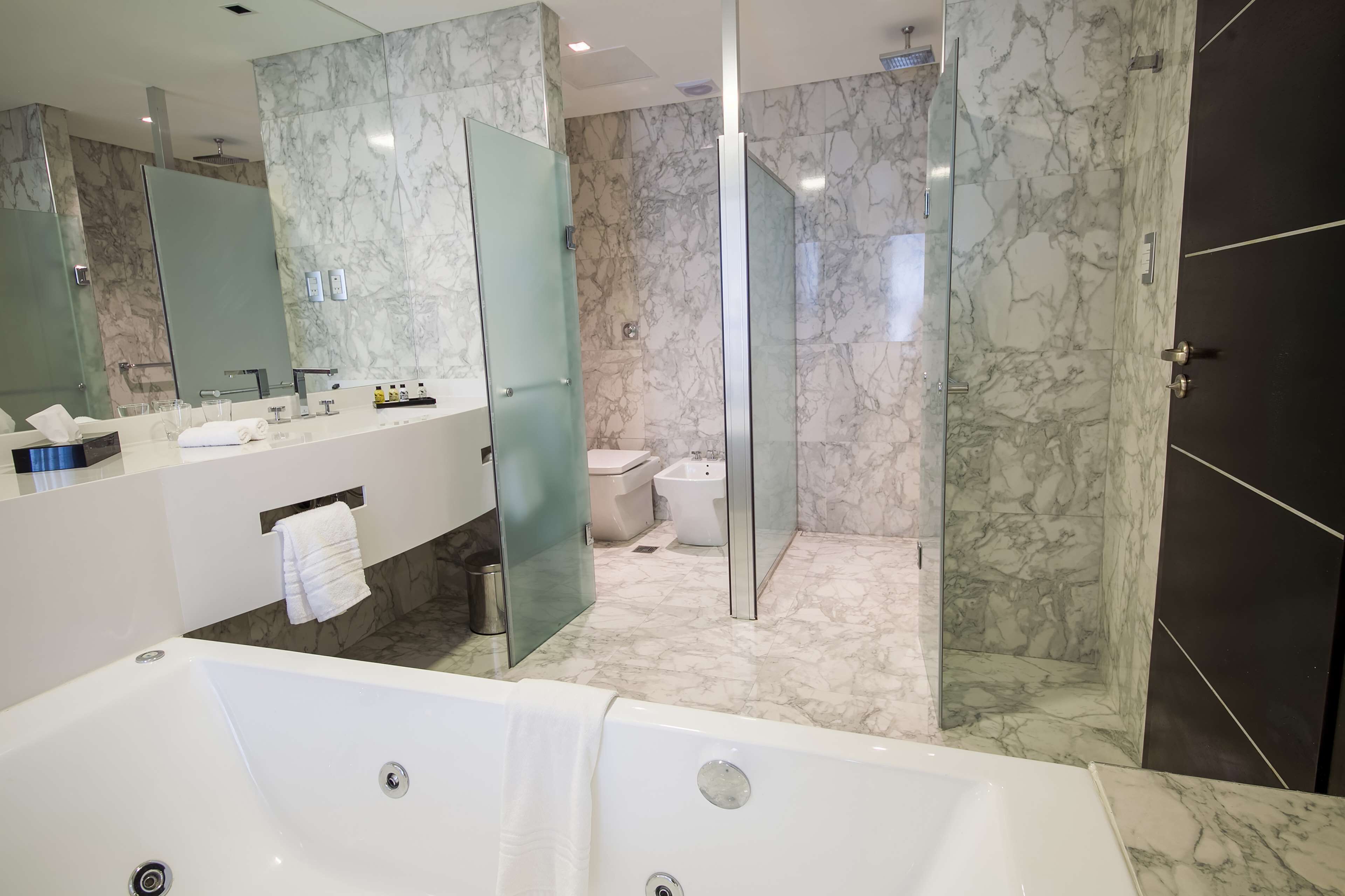 A modern bathroom with a large bathtub, a glass-enclosed shower, and marble walls.