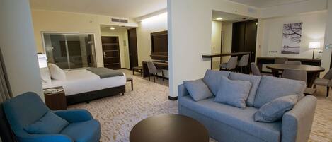 A hotel room with a bed, a sofa, a chair, a small table, and a TV.
