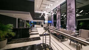 A modern lobby with a checkered floor, a reception desk, seating area, and a staircase.