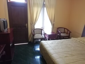 A hotel room with a bed, a desk, two chairs, a television, and a door. - Super OYO 90382 Hotel Sarah Sukabumi (Sukabumi)