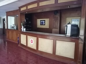 A reception desk with a clock, framed picture, and a television. - Super OYO 90382 Hotel Sarah Sukabumi (Sukabumi)