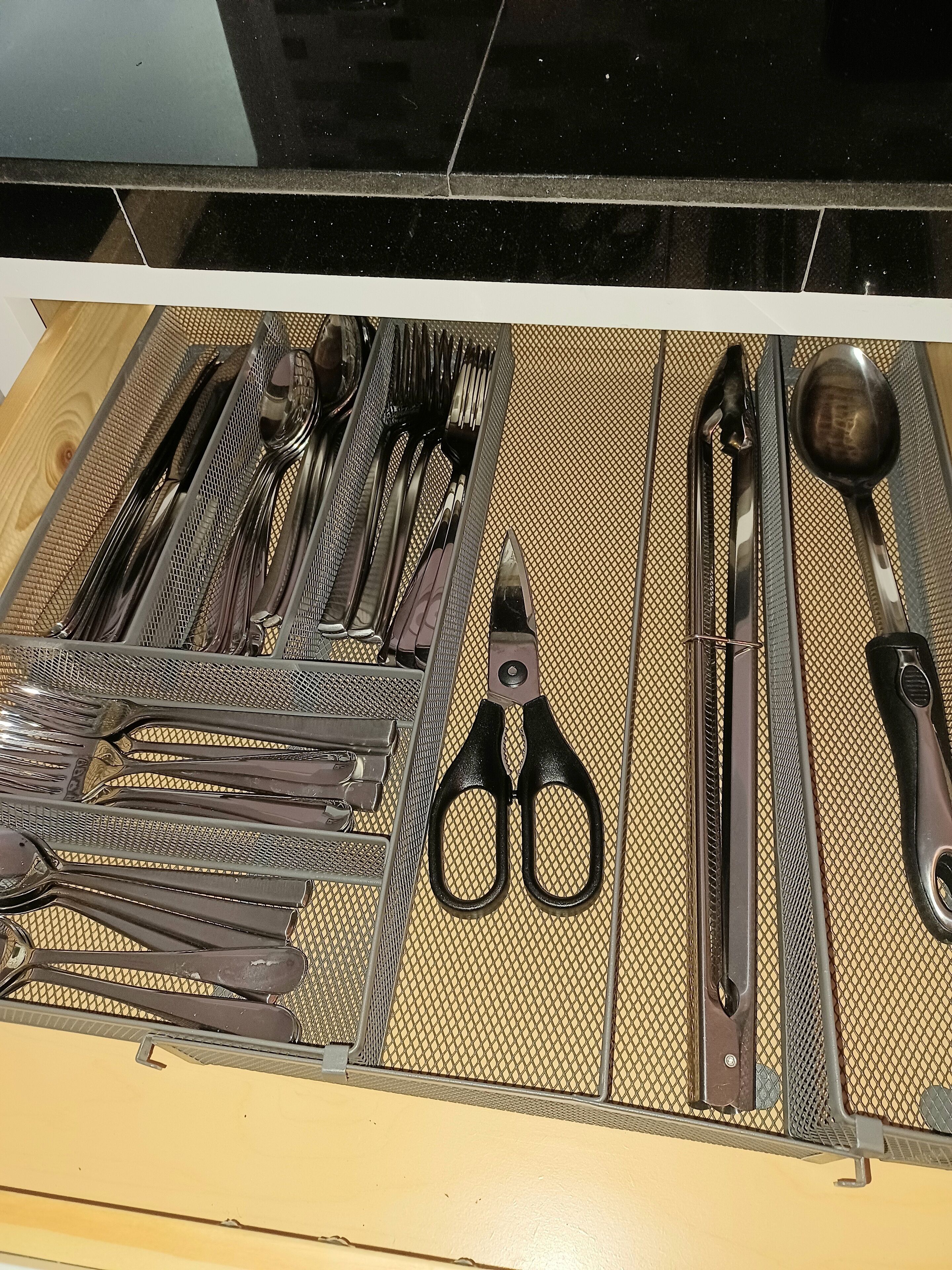 Een lade met een bestekorganizer met diverse keukengereedschappen, zoals een schaar, een tang en een lepel.