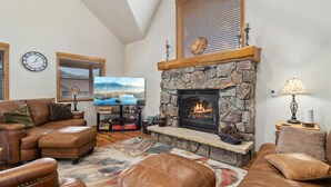 Una sala de estar acogedora con muebles de cuero, una chimenea de piedra, un televisor y un reloj en la pared.