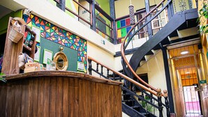 Een meerlaags interieur met een houten toonbank, kleurrijke geometrische wanddecoratie en een spiltrap.