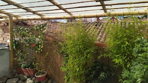 Een pergola van bamboe met potplanten en een bakstenen muur op de achtergrond.