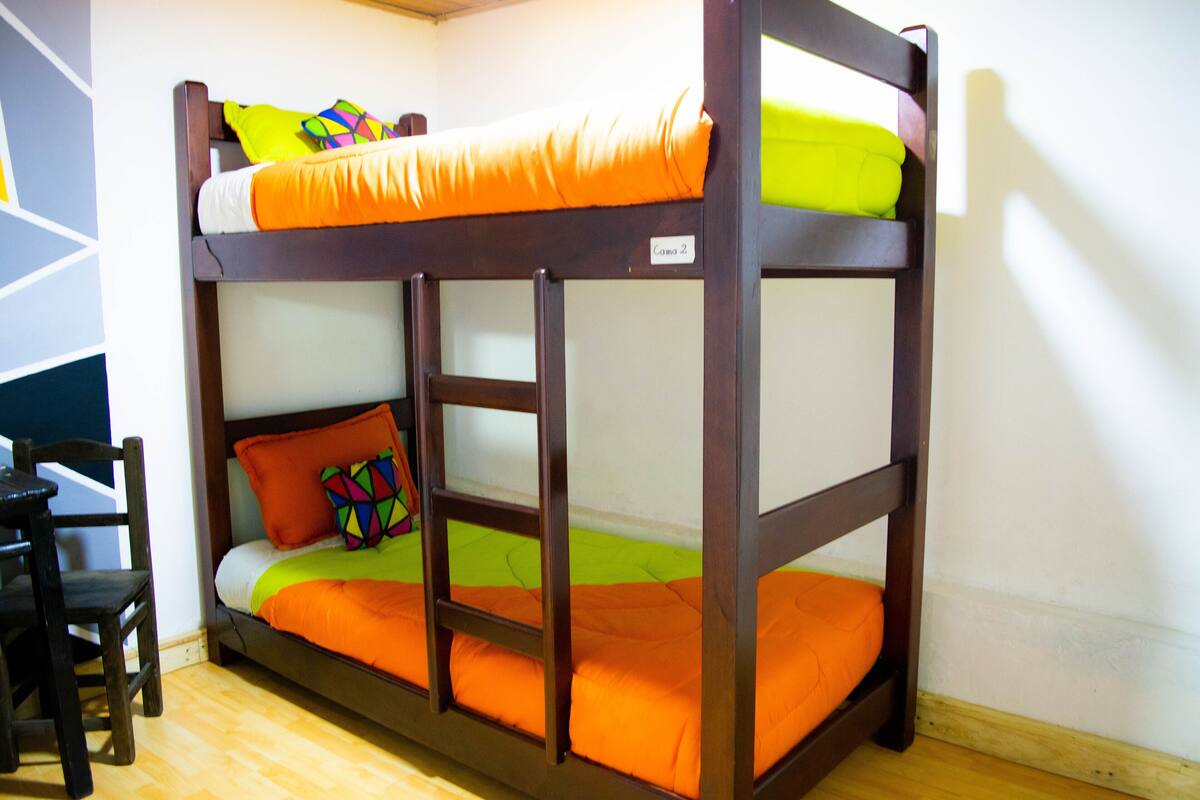 Ein Stockbett mit orangefarbener Bettwäsche, einem farbenfrohen Kopfkissen und einem Holzstuhl.