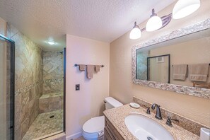 A bathroom with a glass-enclosed shower, a toilet, and a sink with a mirror above. - Southpoint 506 in Ponce Inlet, FL (Ponce Inlet)