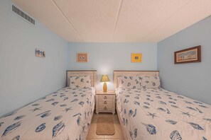 A bedroom with two single beds, a nightstand with a lamp, and a small rug. - Southpoint 506 in Ponce Inlet, FL (Ponce Inlet)