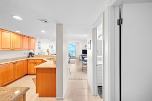 A modern kitchen with wooden cabinets, a granite countertop, and a view to the living area. - #506 Southpoint 2/2 Oceanfront Condo (Ponce Inlet)