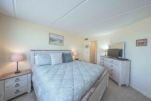 A bedroom with a bed, bedside tables, a dresser, a mirror, and a painting on the wall. - Southpoint 506 in Ponce Inlet, FL (Ponce Inlet)