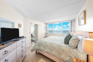 A bedroom with a bed, a TV, a dresser, and a window with a view of the sea. - #506 Southpoint 2/2 Oceanfront Condo (Ponce Inlet)