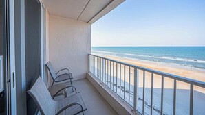 A balcony with a view of the beach, featuring a railing and two chairs.