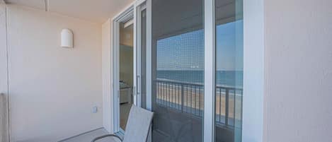 Un balcón con dos sillas, una puerta corrediza de vidrio y vista a la playa.