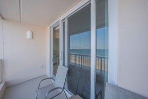 A balcony with two chairs, a sliding glass door, and a view of the beach.