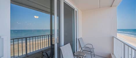 Un balcón con vista a la playa, una puerta de cristal y dos sillas.