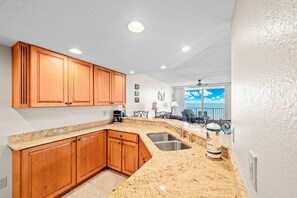 Eine Küche mit Holzausstattung, Granit-Arbeitsplatten, einer Edelstahl-Spüle und Blick auf das Meer vom Balkon aus.