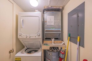 A laundry room with a stacked washer and dryer, a utility panel, and a fire extinguisher.