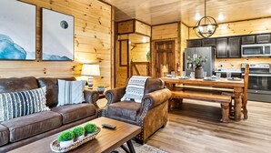Ein gemütliches Blockhauss-Interieur mit Holzvertäfelung, einer Ledersofa, einem Esstisch und einer Küchenzeile.