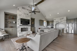 A spacious living area with a stone fireplace, a large gray sofa, a wooden coffee table, and a TV mounted on the wall.