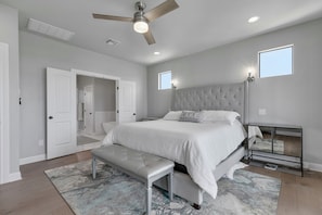 A bedroom with a large bed, a bench, a ceiling fan, and a nightstand.