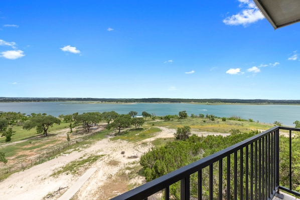 A balcony with a view of a lake, trees, and a distant shoreline.
