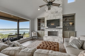 A modern living room with a stone fireplace, a flat-screen TV, and a large window overlooking a scenic view.
