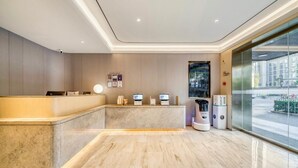A modern reception area with a marble counter, digital check-in stations, and a view of the street through large windows. - JI Hotel (Hangzhou West Lake Hubin Jiefang Road) (Hangzhou)