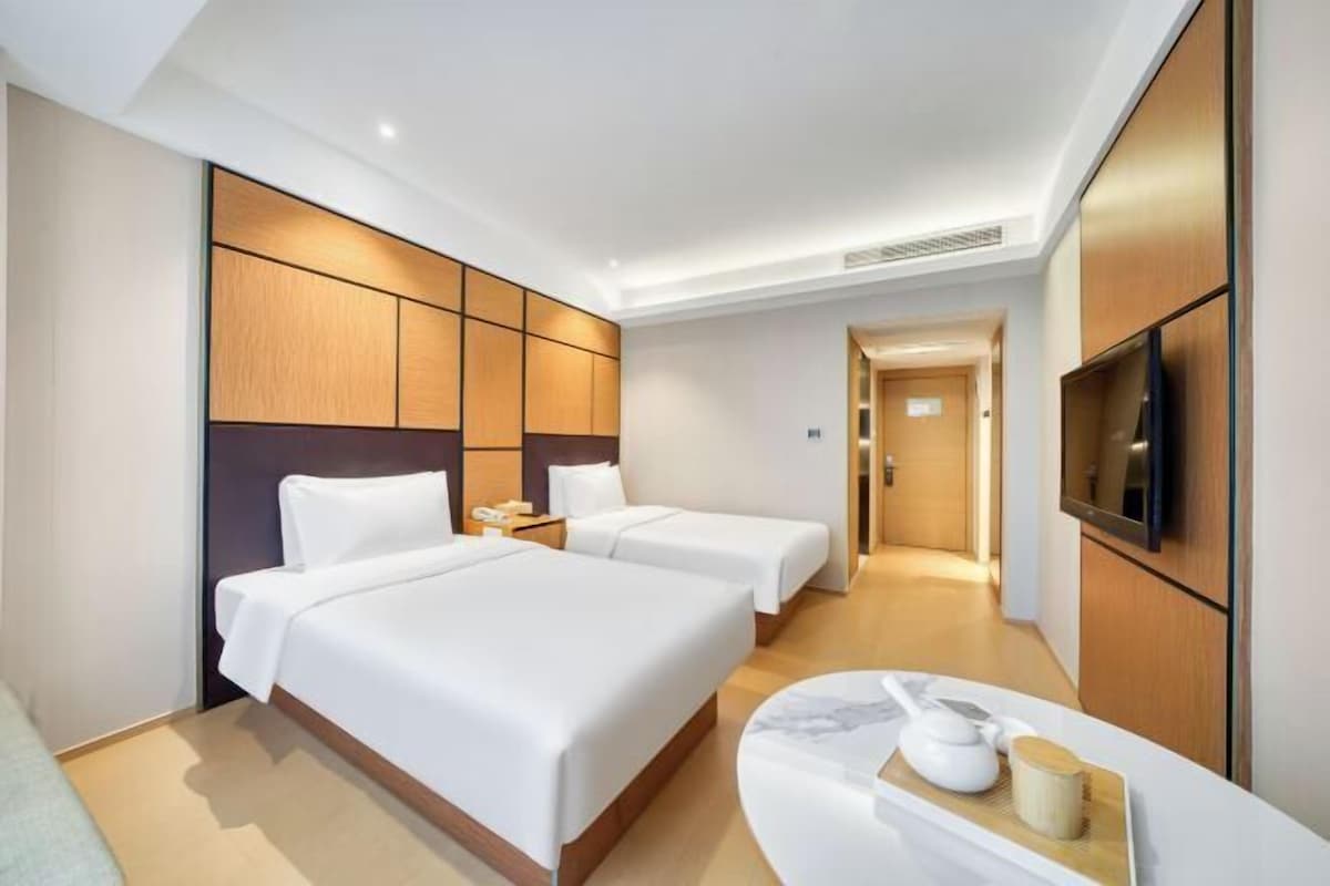 A hotel room with two beds, a TV, a bedside table with a tray, and a wooden headboard.