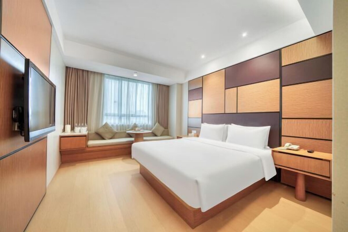 A modern hotel room with a large bed, a TV, a seating area, and a wooden accent wall.