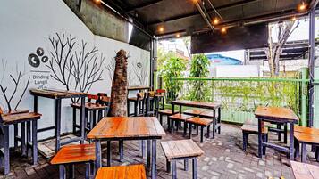 An outdoor seating area with wooden tables and benches, a mural on the wall, and a green fence in the background.