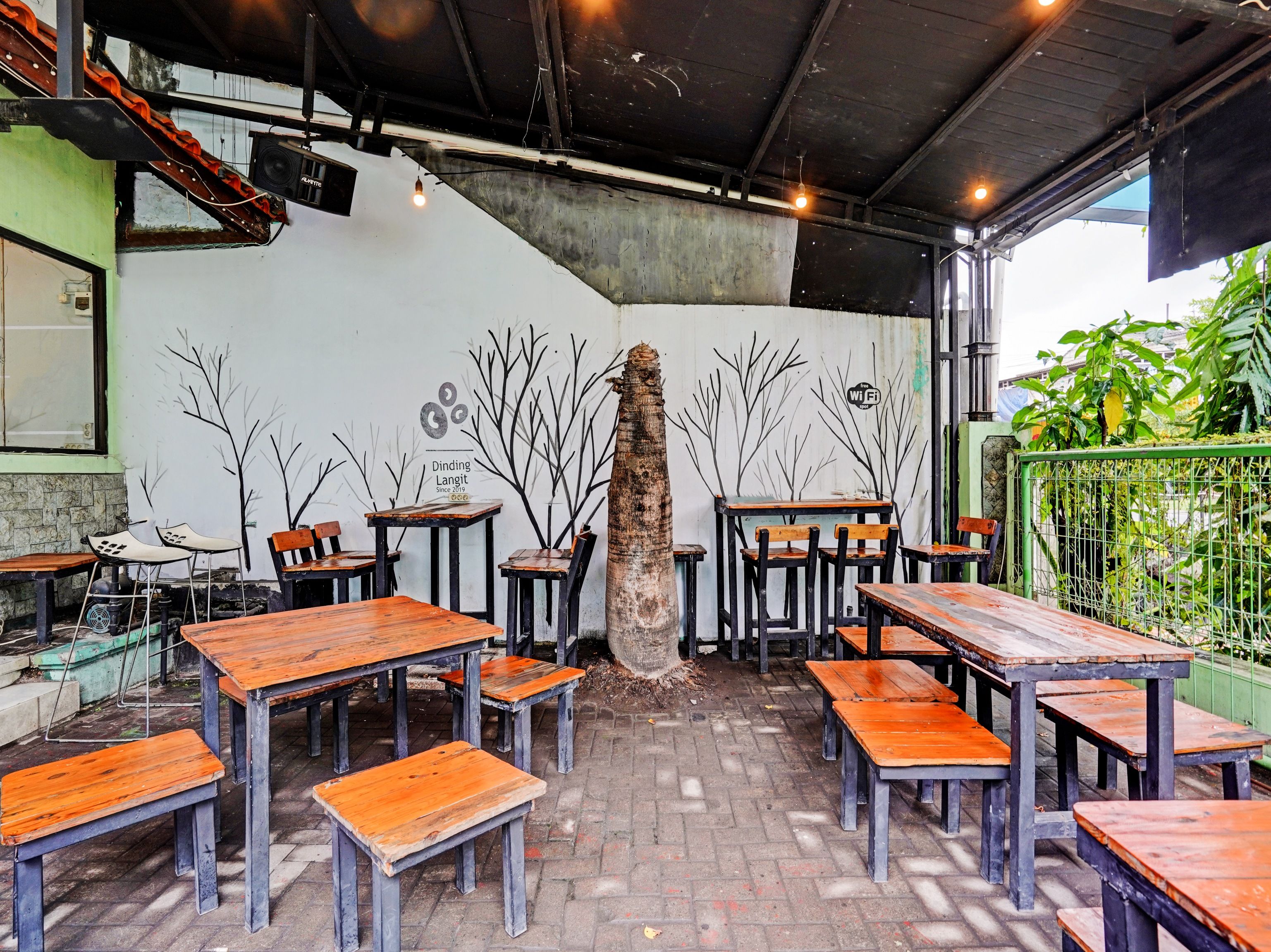 A restaurant interior with wooden tables and chairs, a concrete pillar, and a mural with abstract tree designs.