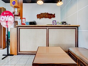 A reception desk with a wooden counter, a sign above it, and a seating area with a bench. - OYO 90361 Griya Noumi Syariah (Surabaya)