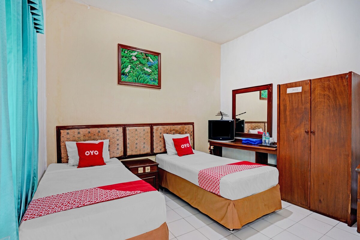 A hotel room with two beds, a television, a wardrobe, and a painting on the wall.