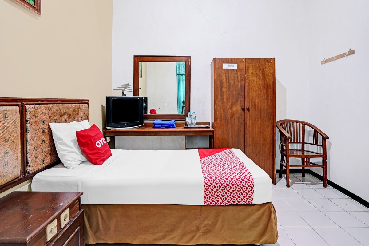 Una habitación de hotel con una cama, un escritorio con computadora, una silla, un armario y un espejo.