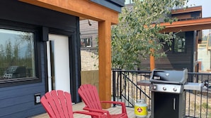 A deck with red Adirondack chairs, a grill, and a gas canister. - Luxury. Steps to the Timberline Chairlift (Fernie)